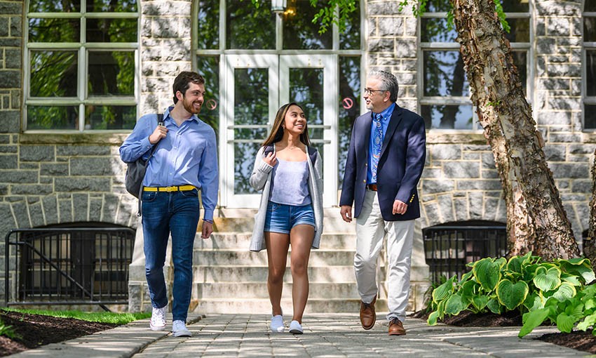 Faculty member walking with two èƵapp students outside Tolentine Hall.
